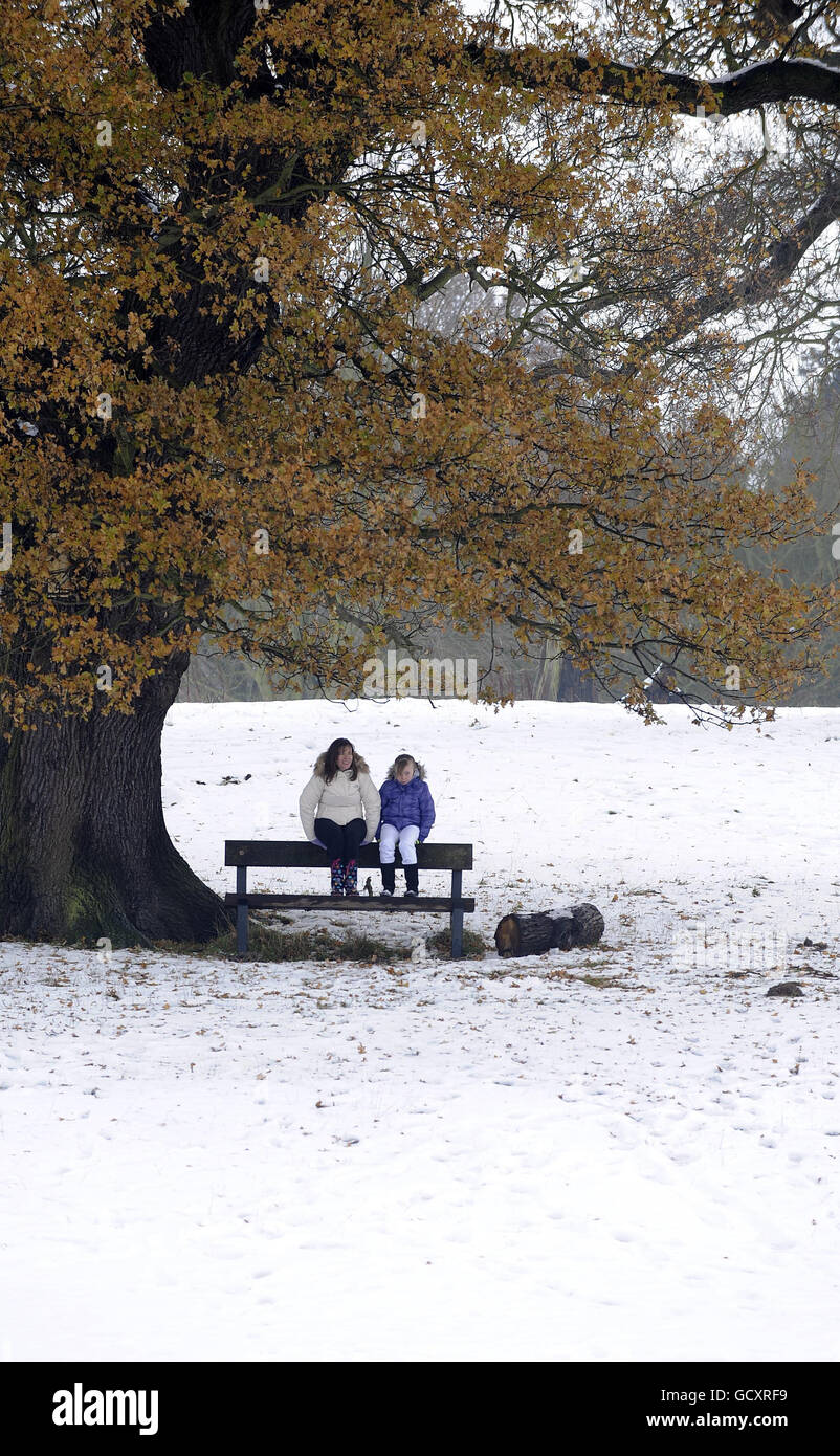 A woman and girl sit under a tree on a bench in the remaining snow in