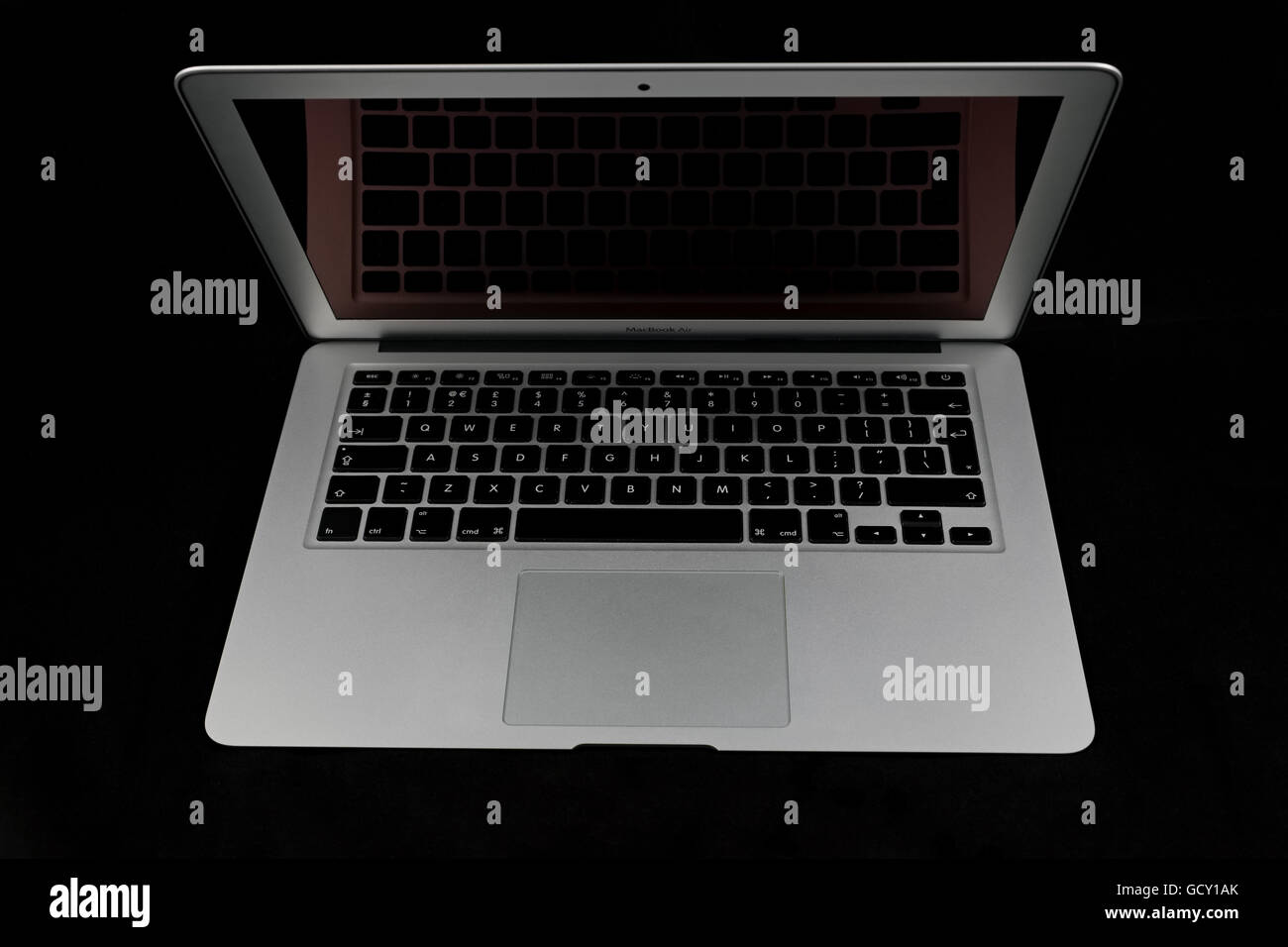 An open Apple MacBook Air mid 2012 on a black background with a blank screen showing a reflection of the keyboard. Stock Photo