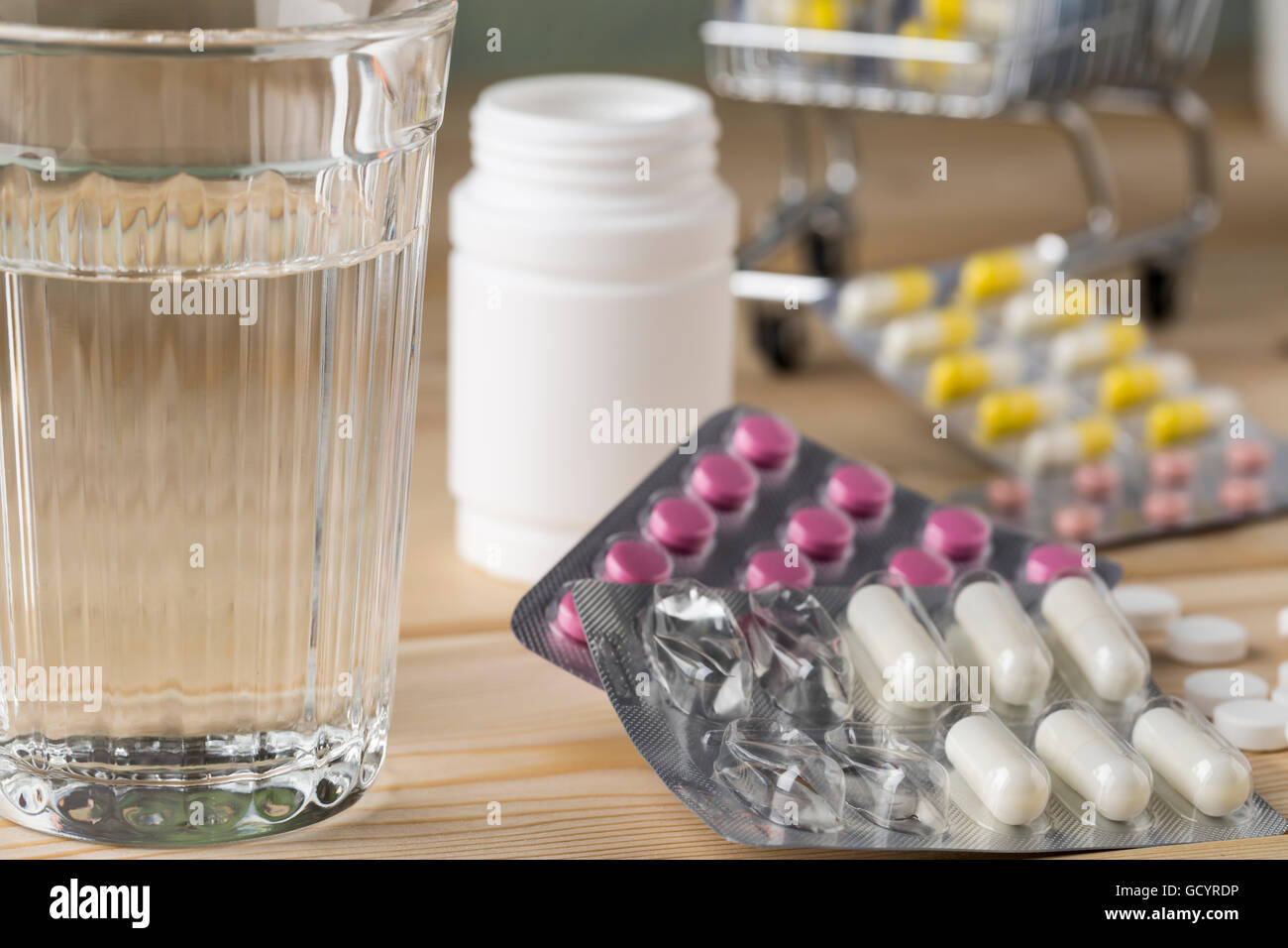 Glass of clean water and a bunch of packs of colorful pills and capsules Stock Photo