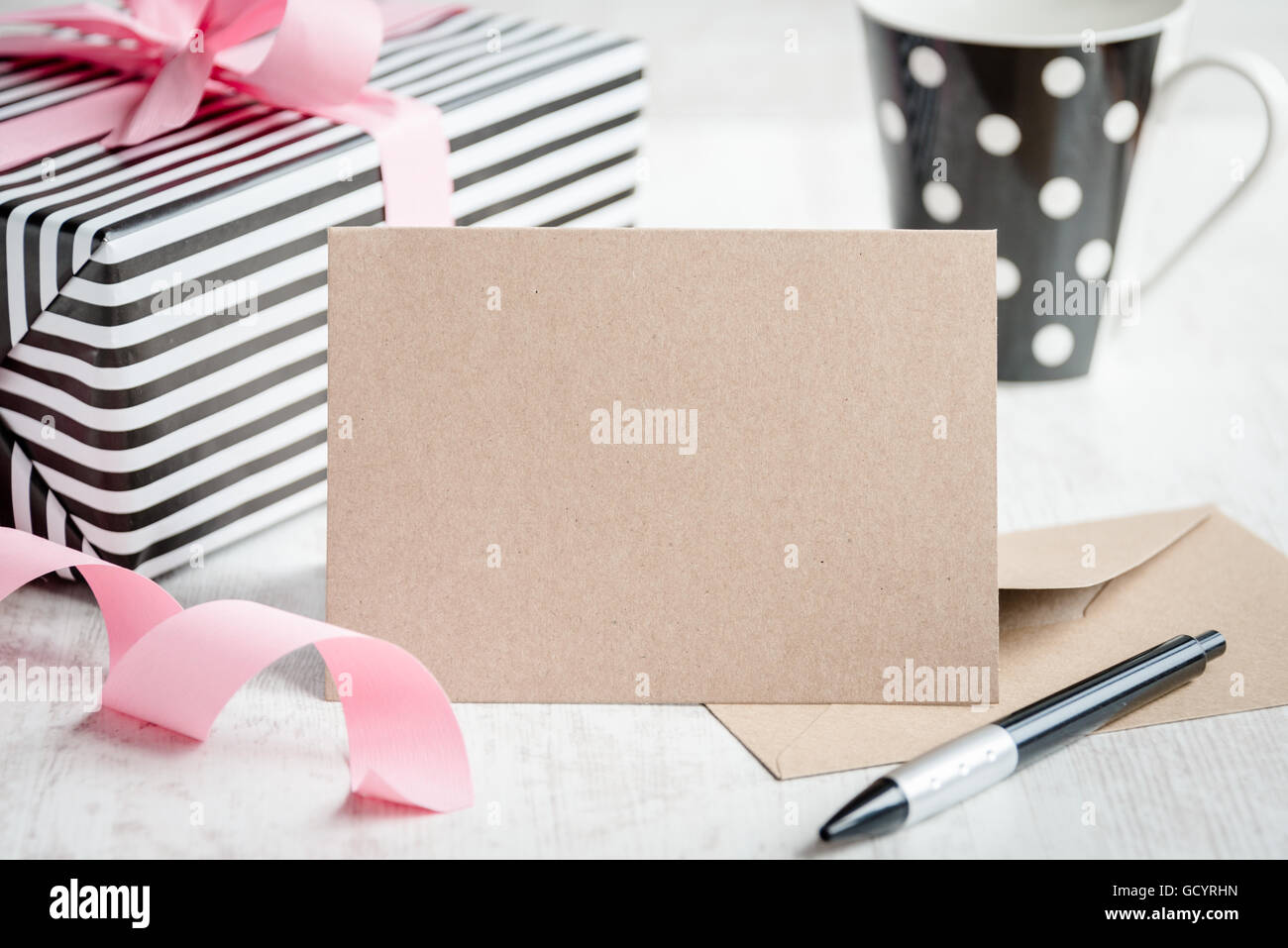 Empty greeting kraft card. Wrapped gift and coffee cup in the background. Stock Photo