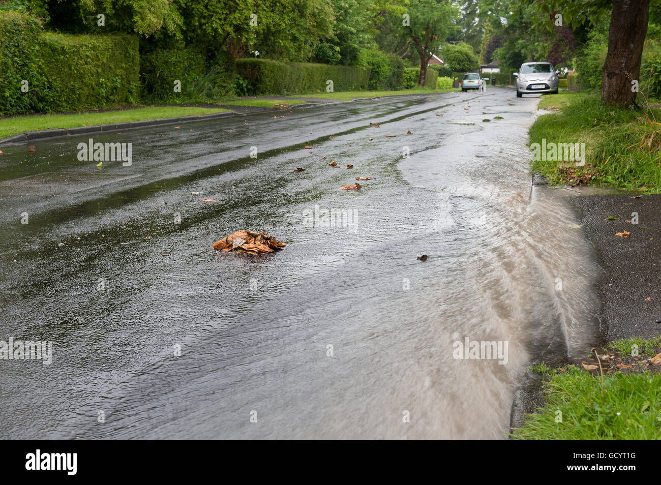 fast flowing stream produced after torrential thunder and sheets of heavy rain creates gushing soaked road surface weather Stock Photo