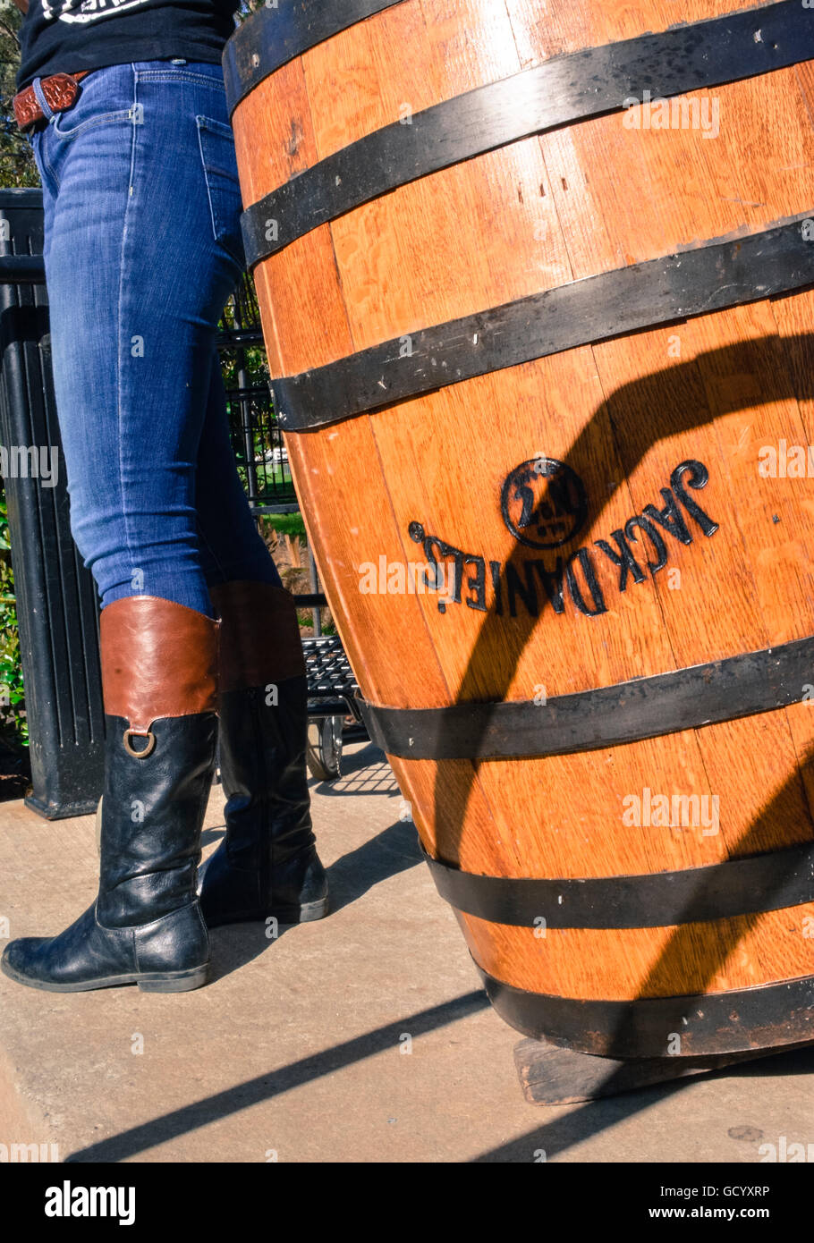 A Woman's legs in tight jeans tucked into riding boots along side an upside down Jack Daniel's oak barrel with metal bands Stock Photo