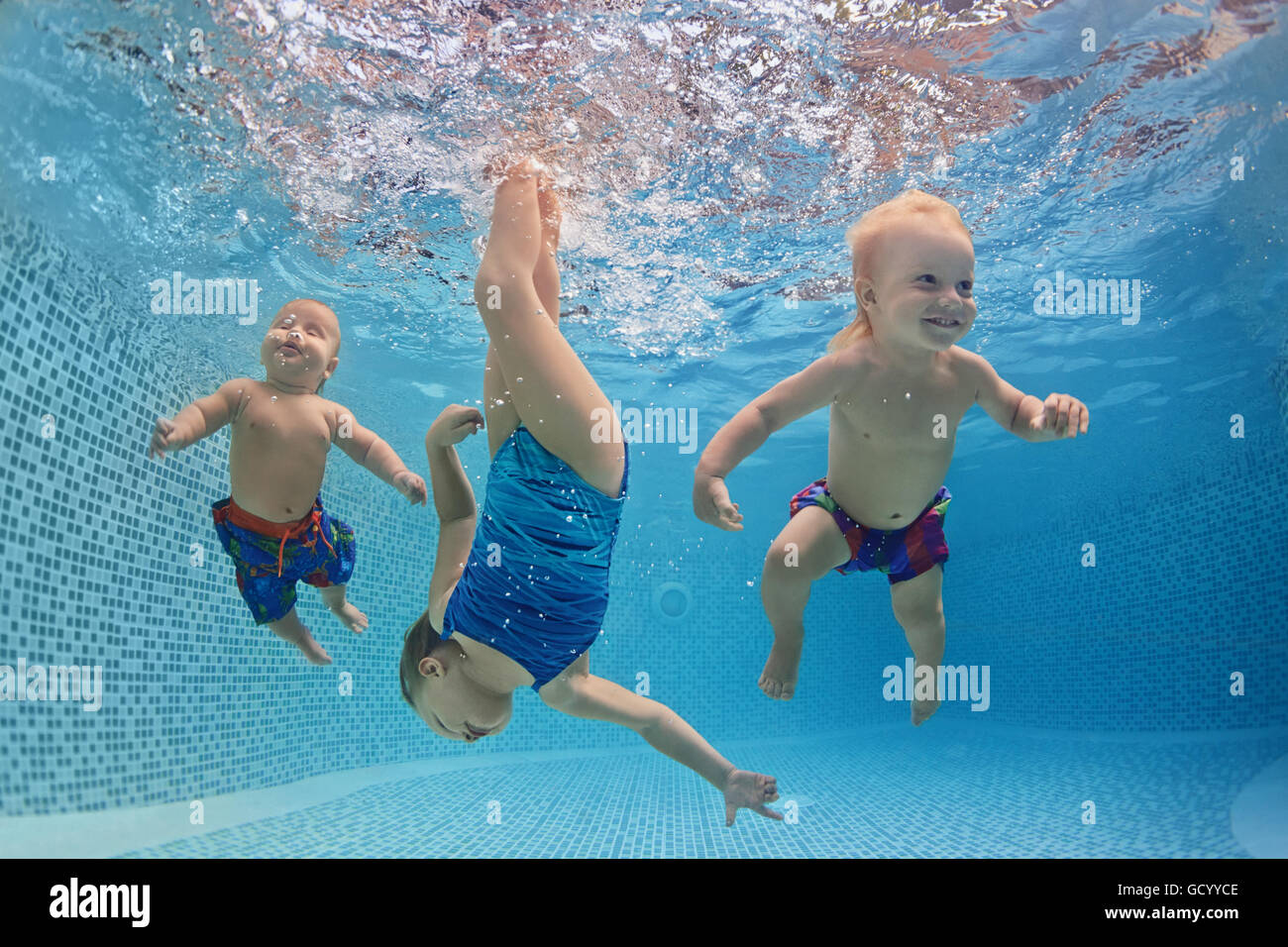 Funny photo of active babies swim and dive with fun - jump deep down underwater with splashes in swimming pool. Stock Photo