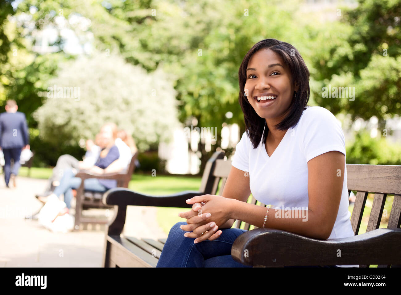 happy young woman sitting on a park bench Stock Photo - Alamy