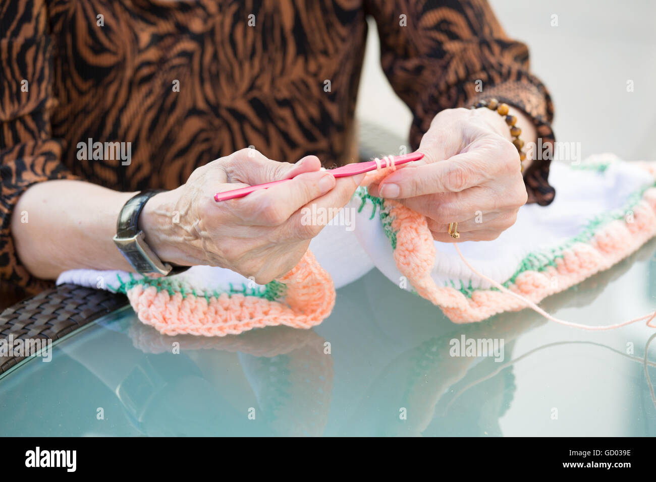 Closeup cropped portrait of old woman hands, sitting and crocheting cloth with orange needles, isolated outdoors background Stock Photo