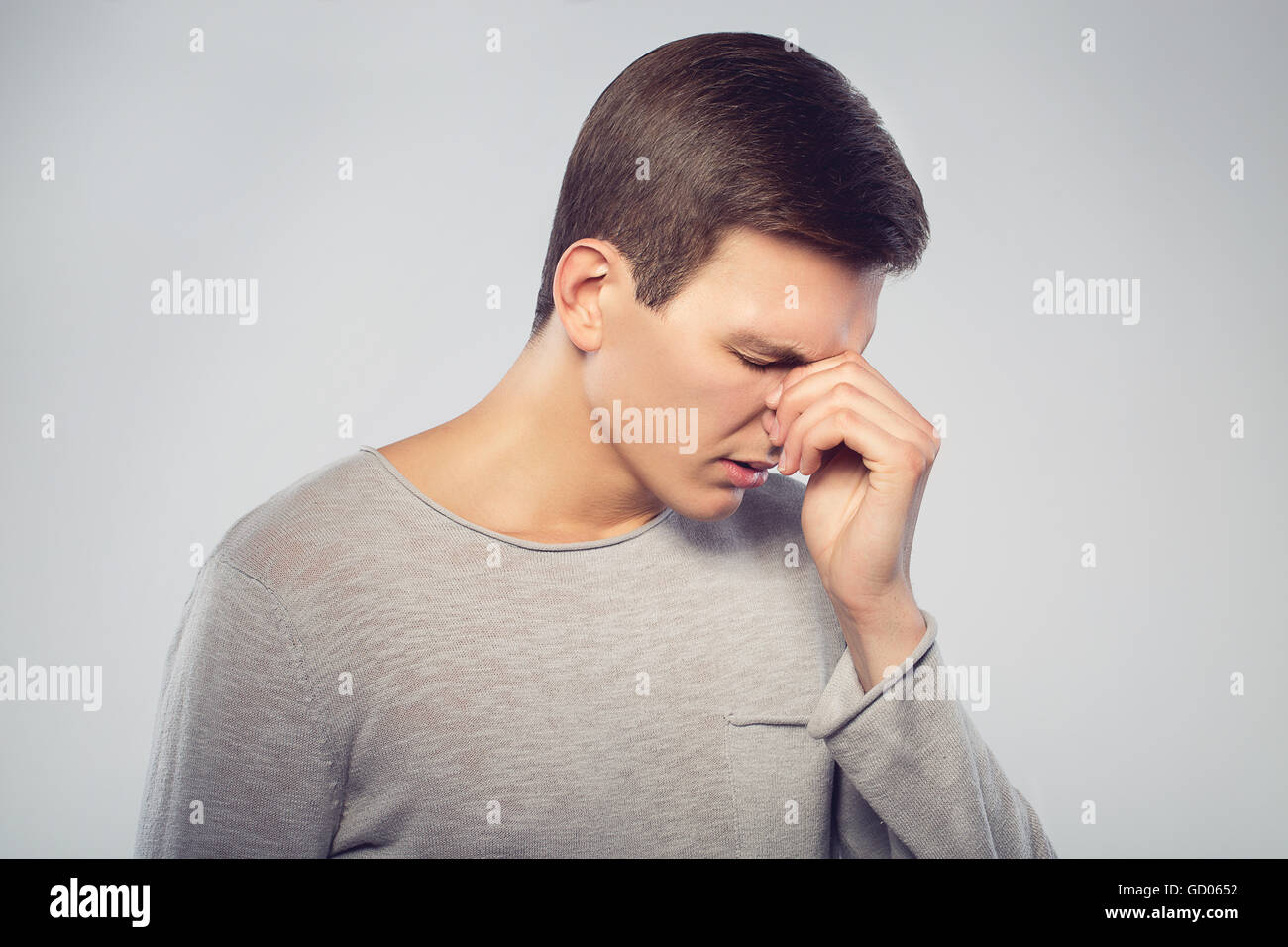 Feeling sick and tired. Frustrated young man massaging his nose and keeping eyes closed isolated on gray background Stock Photo