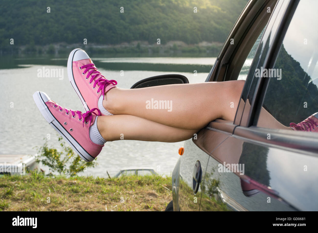 Woman legs out of the car window by the lake Stock Photo