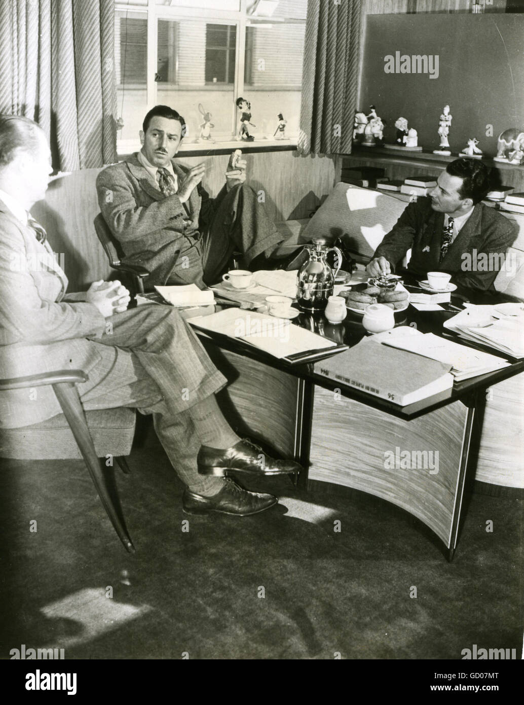 Production conferences begin as Walt Disney downs doughnuts and coffee in his office. With Disney are production manager Harry Teitel (left) and editor Hal Adelquist. Stock Photo