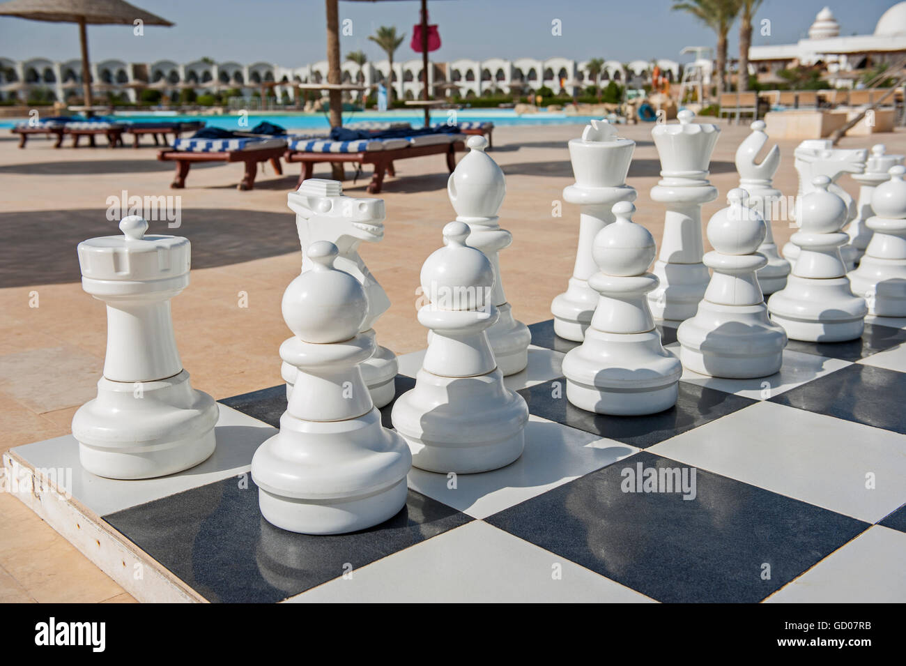 Closeup of playing pieces on giant chess boards game in tropical hotel resort with swimming pool Stock Photo