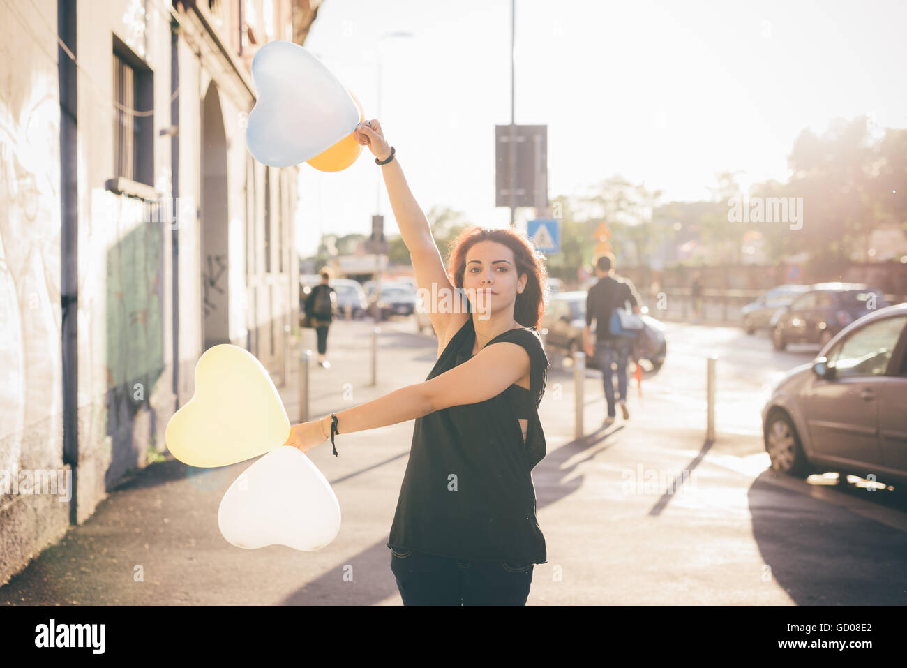 Half length of a young reddish brown hair caucasian woman playing in the street with baloon in shape of heart - youth, childhood, carefreeness concept - dressed with black shirt Stock Photo