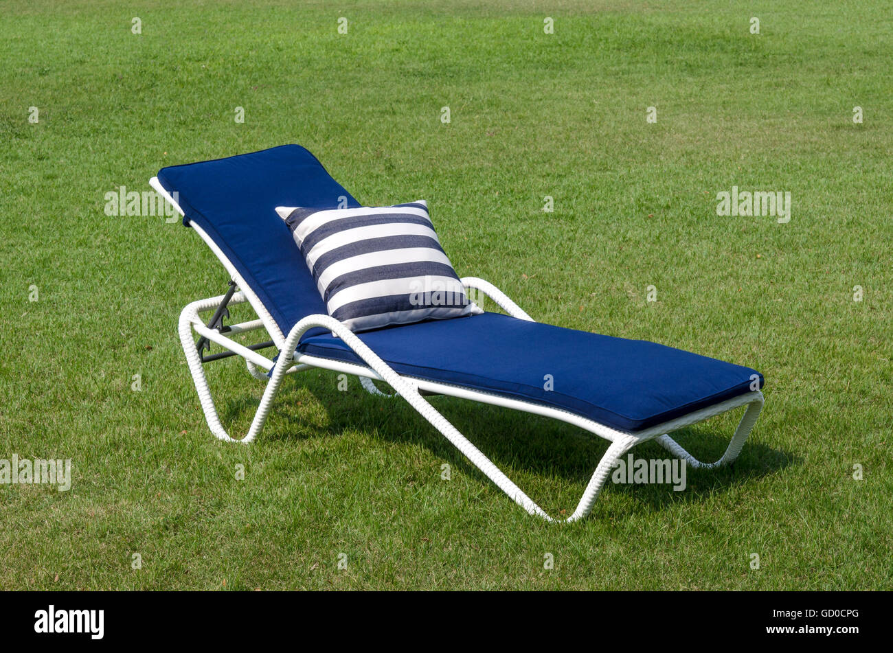 White rattan sun lounger with blue cushion and pillow in the garden Stock Photo