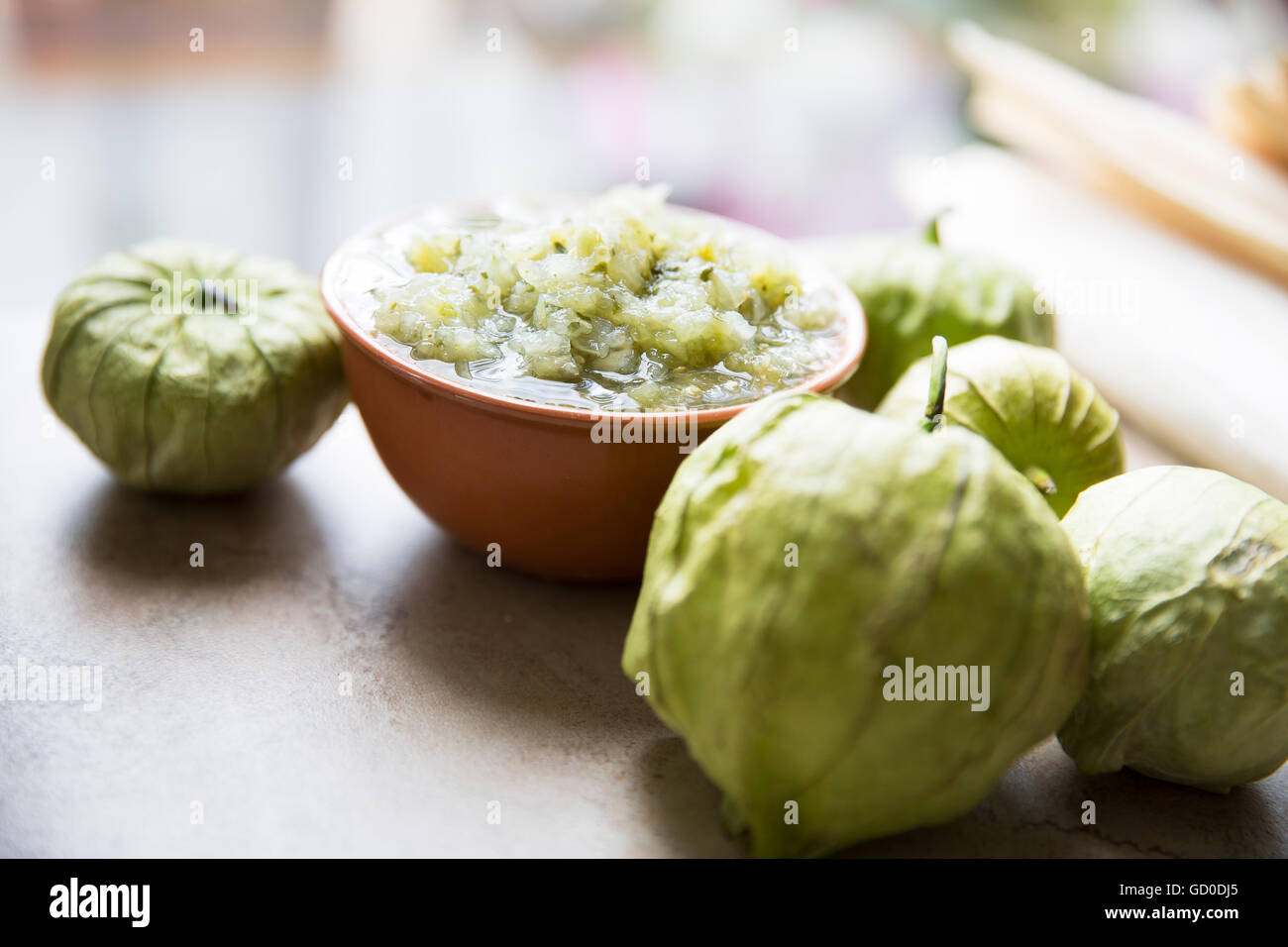 Tomatillos and  a bowl of green salsa on stone surface. Stock Photo