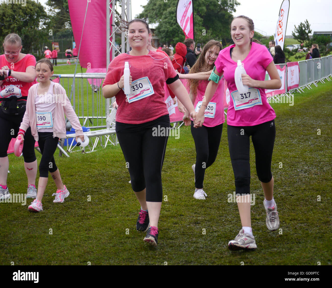 Portsmouth, Hampshire, UK. 10 July 2016. Two friends cross the finish line holding hands, at the end of the Race for life. The Race for life is a charity event in which females complete a 10Km or 5Km run in aid of cancer reseach. Credit:  simon evans/Alamy Live News Stock Photo