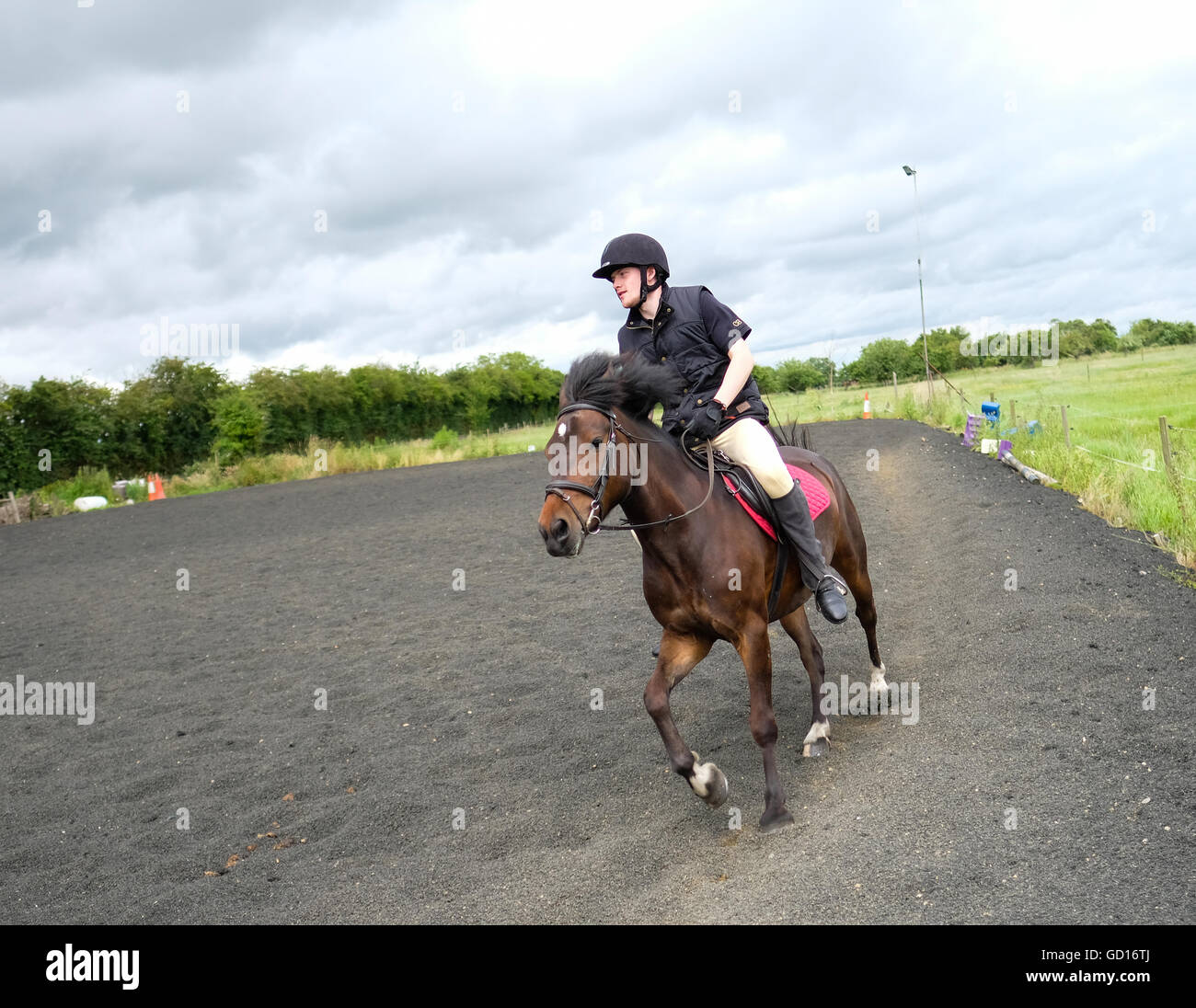 Young man in full equestrian safety gear seen riding a horse in an outdoor location Stock Photo