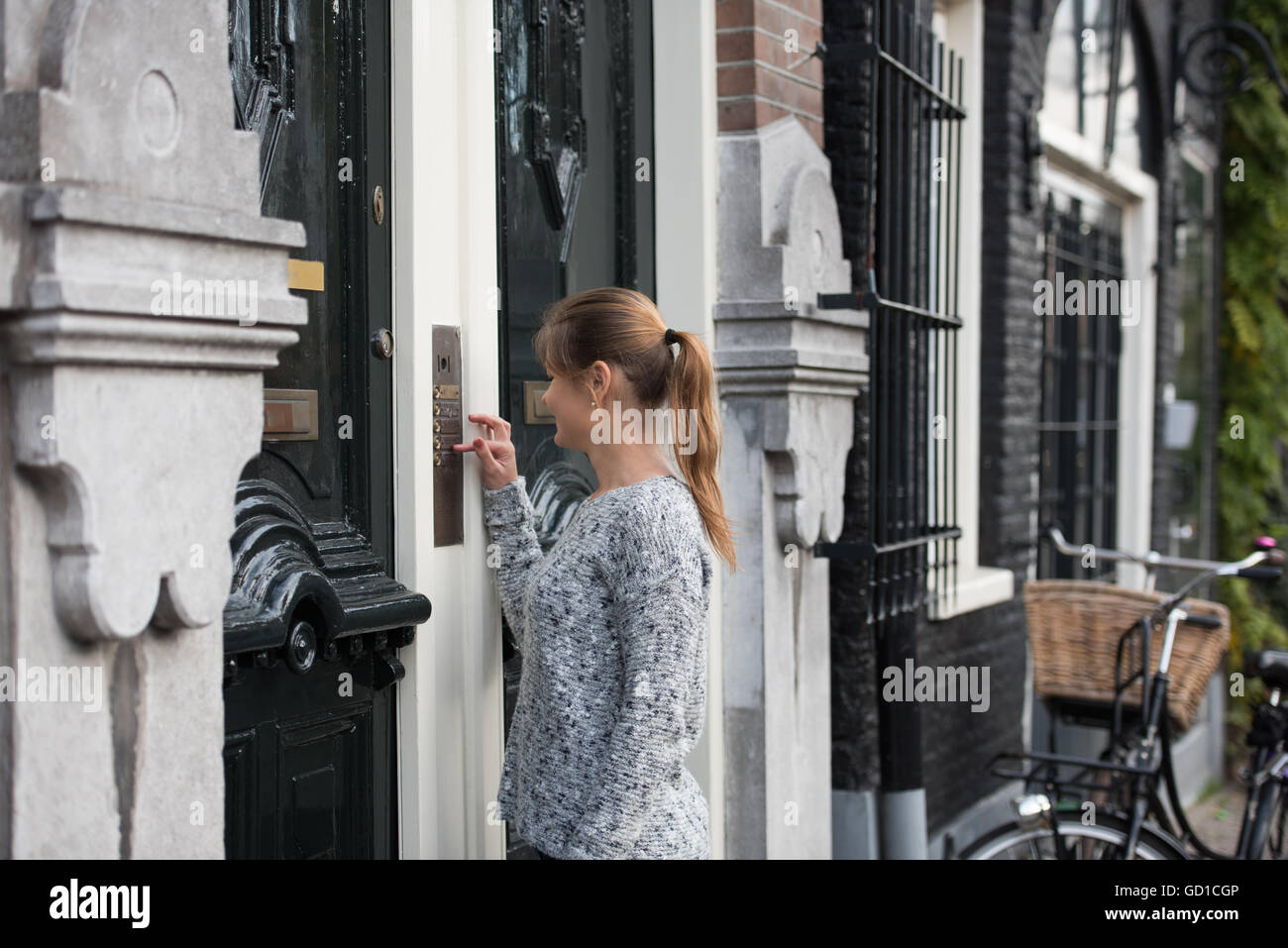 young woman in front of entrance door, ringing at the door bell Stock Photo