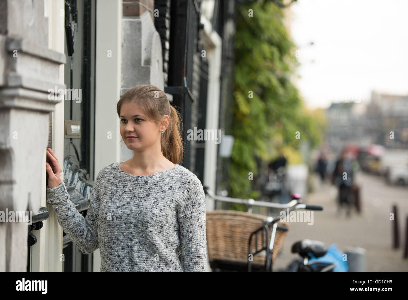 young woman in front of entrance door, ringing at the door bell Stock Photo