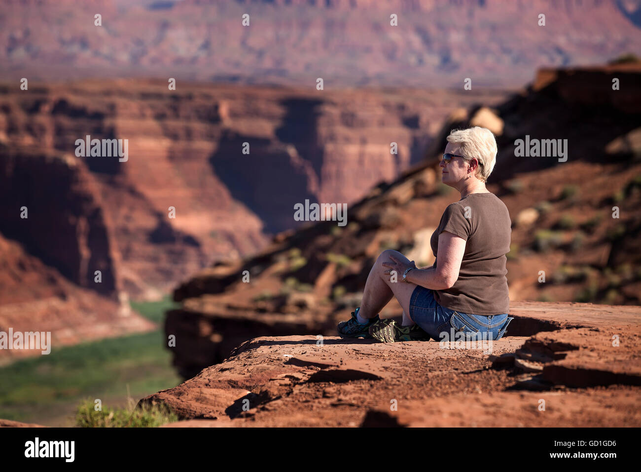 Woman sitting on the edge of a rock canyon cliff looking over the ...