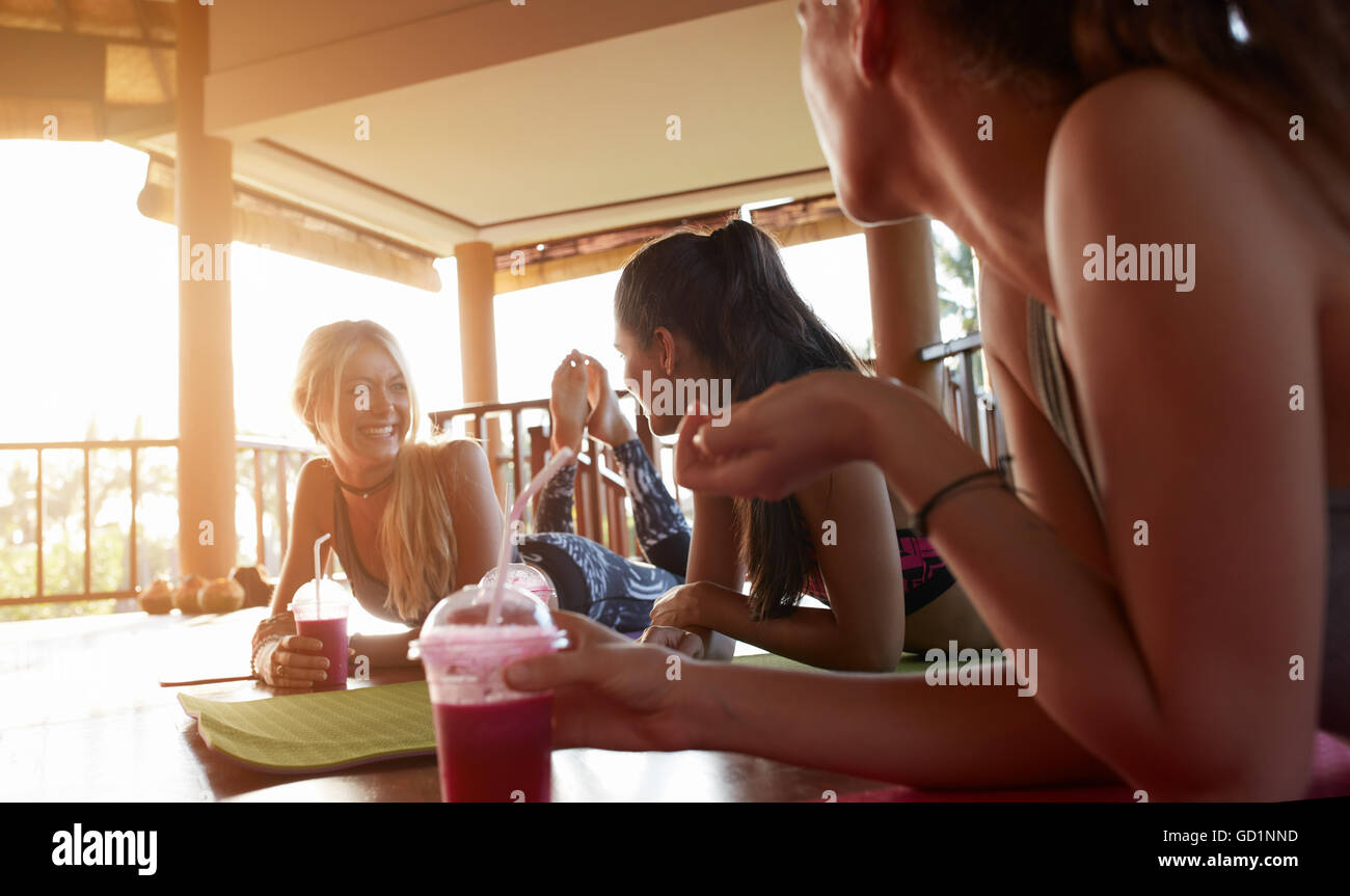 Group of women relaxing with fresh fruit juice after yoga class. Female friends during yoga class break at health club. Stock Photo