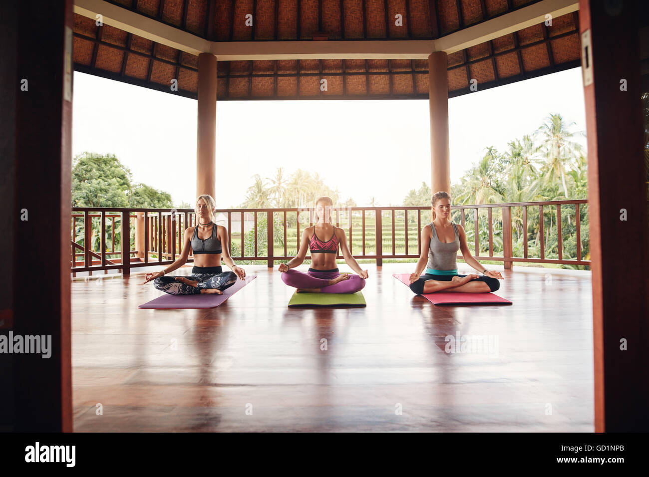 Three women practicing yoga in class. Fitness people sitting in lotus position and meditating at health center. Stock Photo