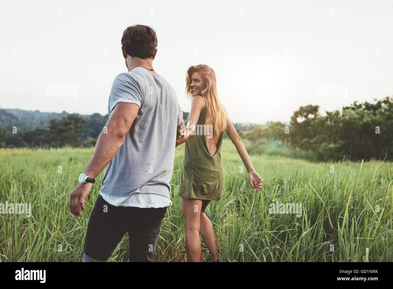 Rear view shot of young woman walking with her boyfriend on grass field. Couple enjoying a walk through grass land. Stock Photo