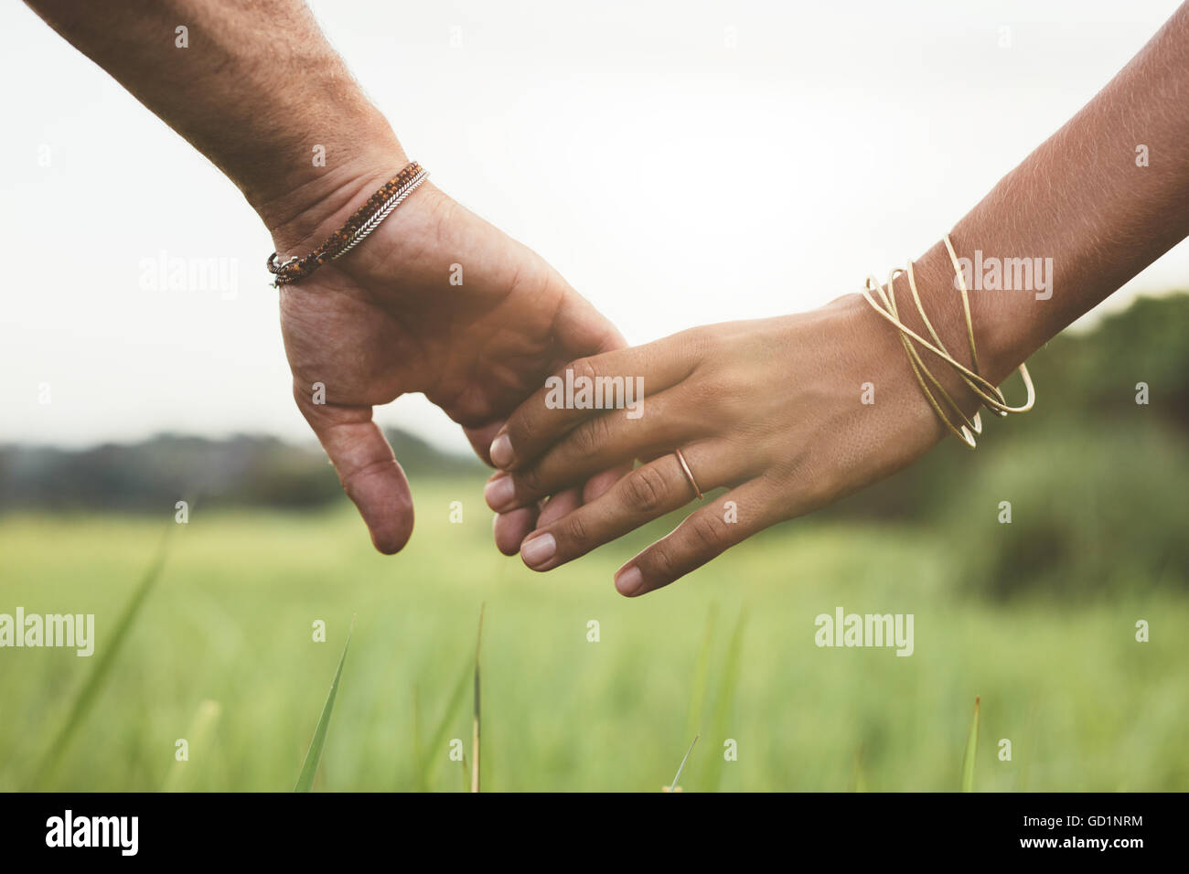 Horizontal shot of young couple walking through meadow holding hands with focus on hands . Stock Photo