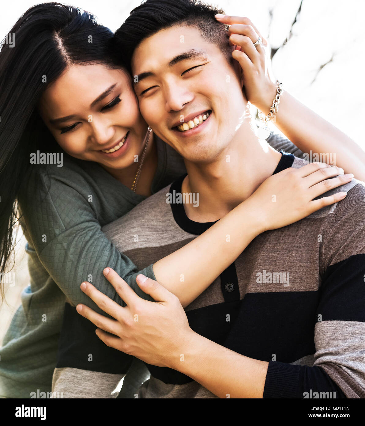 A Young Asian Couple Enjoying Quality Time Together Outdoors In A Park  In Autumn And Embracing Each Other In The Warmth Of The Sunlight During The... Stock Photo