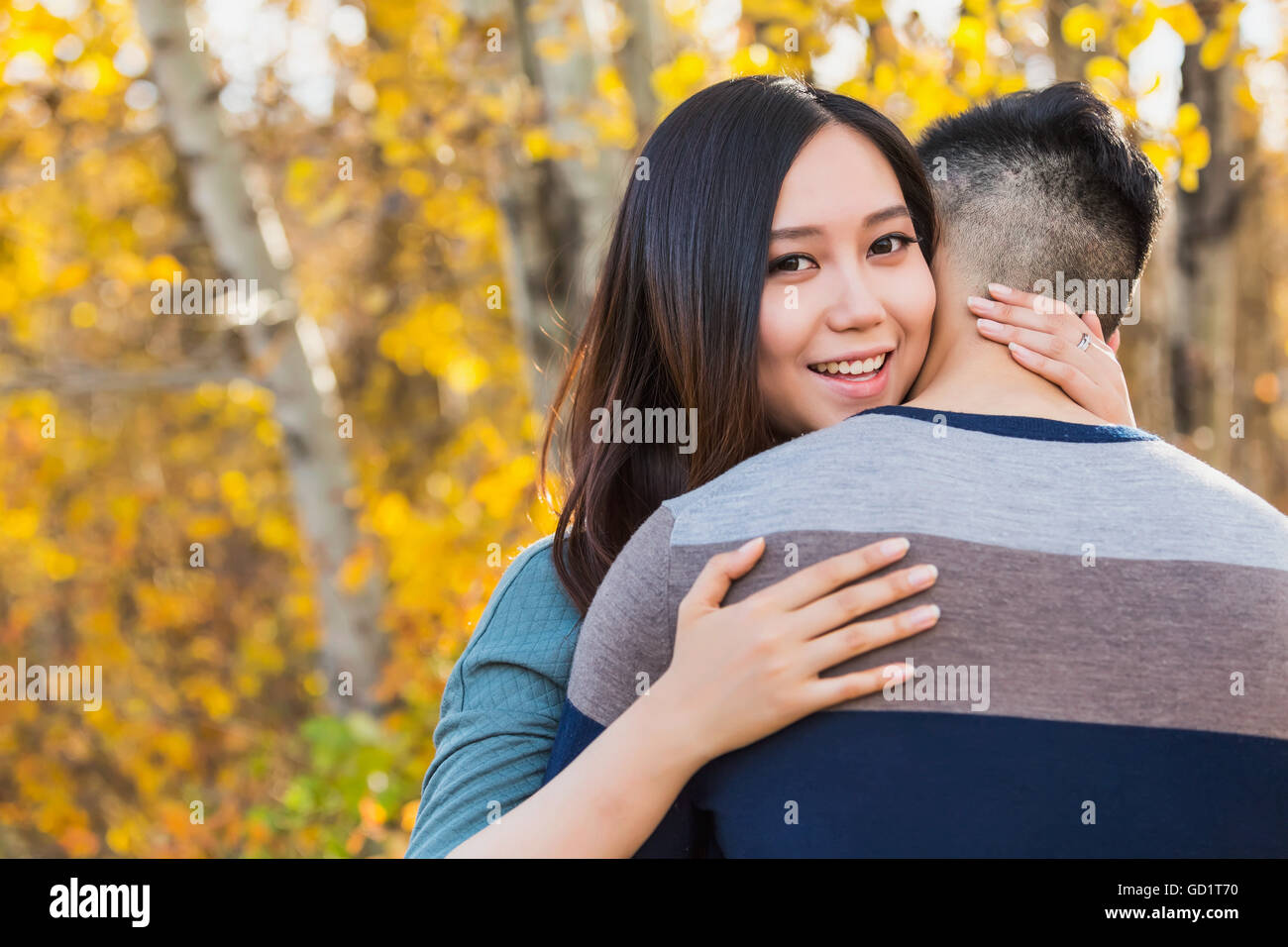 A young Asian woman hugging her boyfriend in a park in autumn and ...