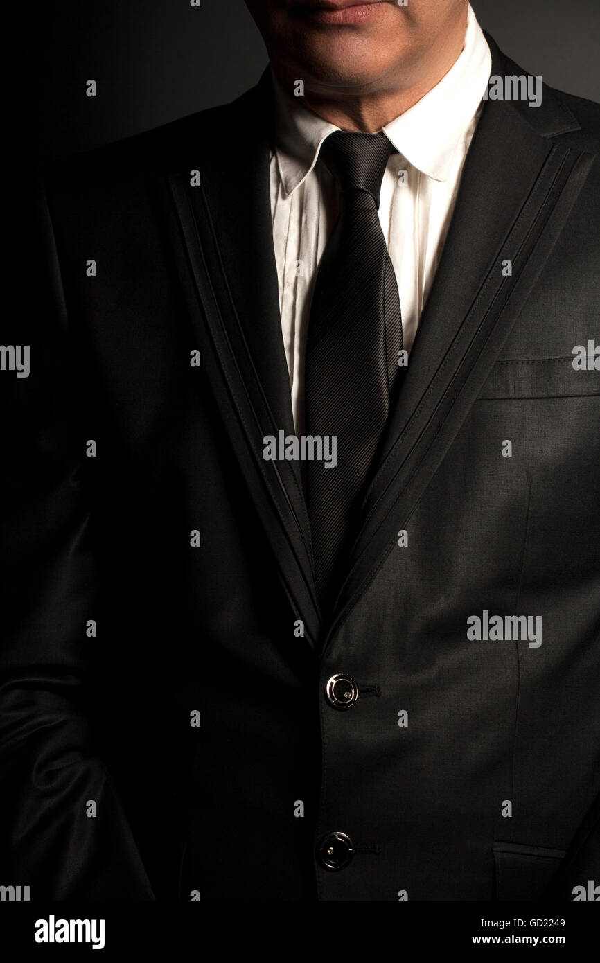 Man in black suit and black tie on a black background Stock Photo - Alamy