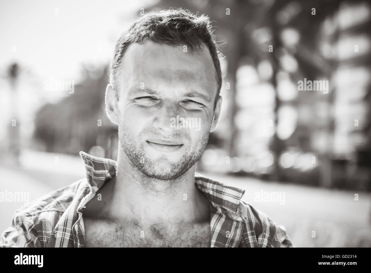 Smiling young handsome Caucasian man, outdoor portrait in sunny day, black and white stylized photo Stock Photo