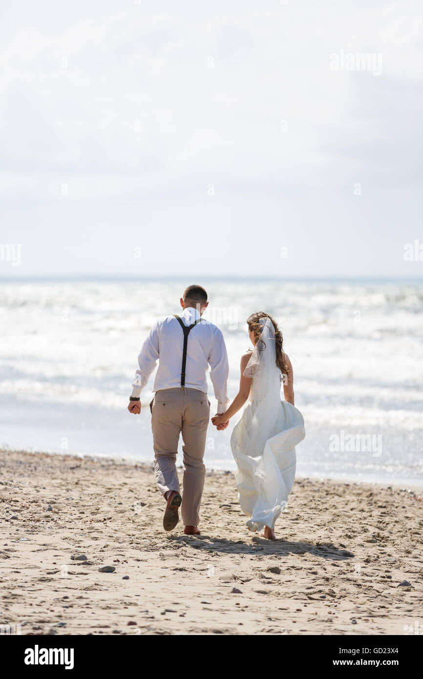 Cheerful wedding couple walking on the beach at summer time Stock Photo
