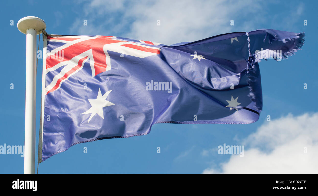 Australian flag blowing in wind on white flag pole with blue sky and ...