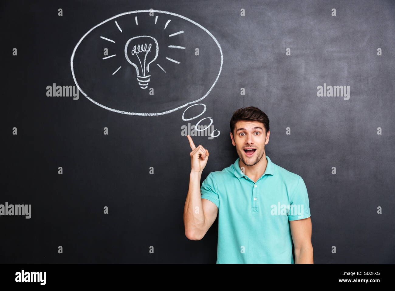 Happy handsome young man pointing up and having an idea over blackboard bakground Stock Photo