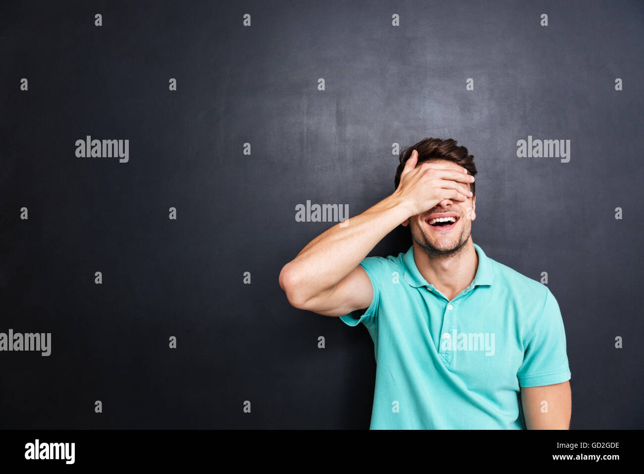 Portrait of a young smiling man covering his eyes with his hand ...