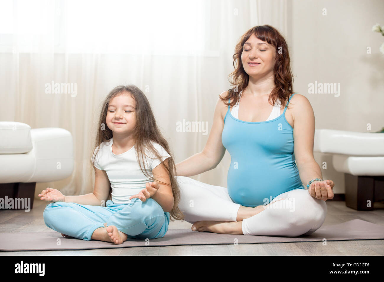 Family healthy lifestyle concept. Pregnancy Yoga and Fitness. Young happy pregnant yoga mom resting after workout with kid girl Stock Photo