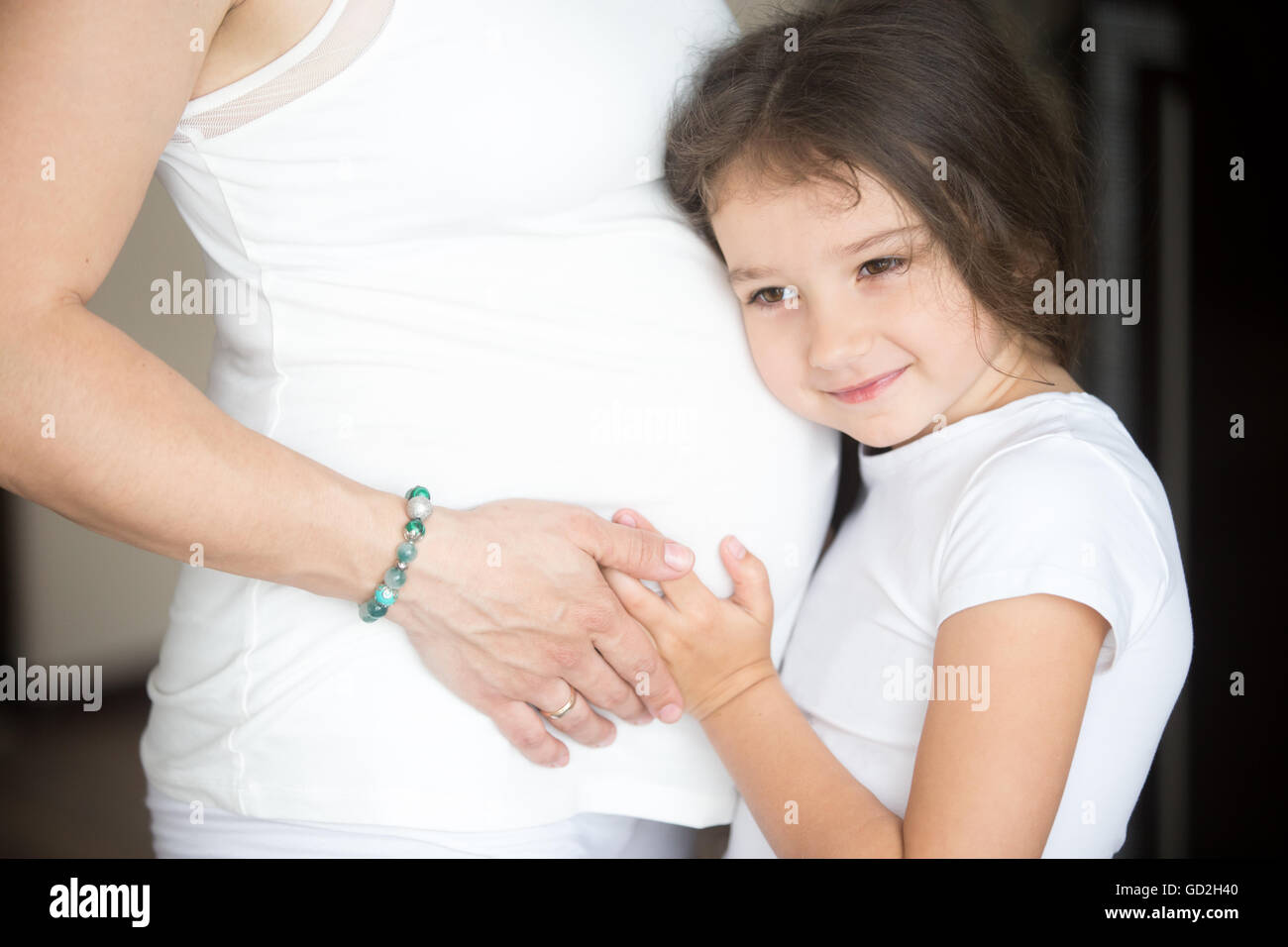 Family lifestyle concept. Adorable little girl hugging her expectant mother belly and listening to baby movements. Young happy Stock Photo