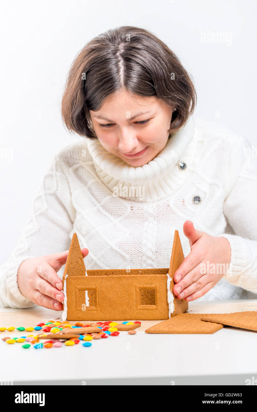 girl in a white sweater making a gingerbread house Stock Photo