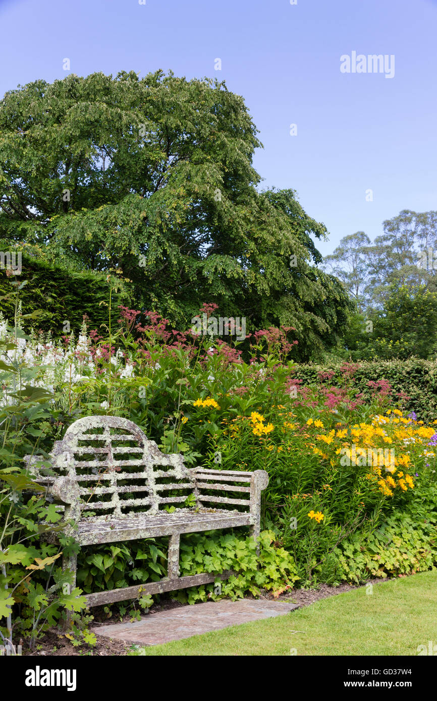 Old, lichen covered Lutyens seat in a herbaceous border at the Garden House, Devon, UK. Stock Photo