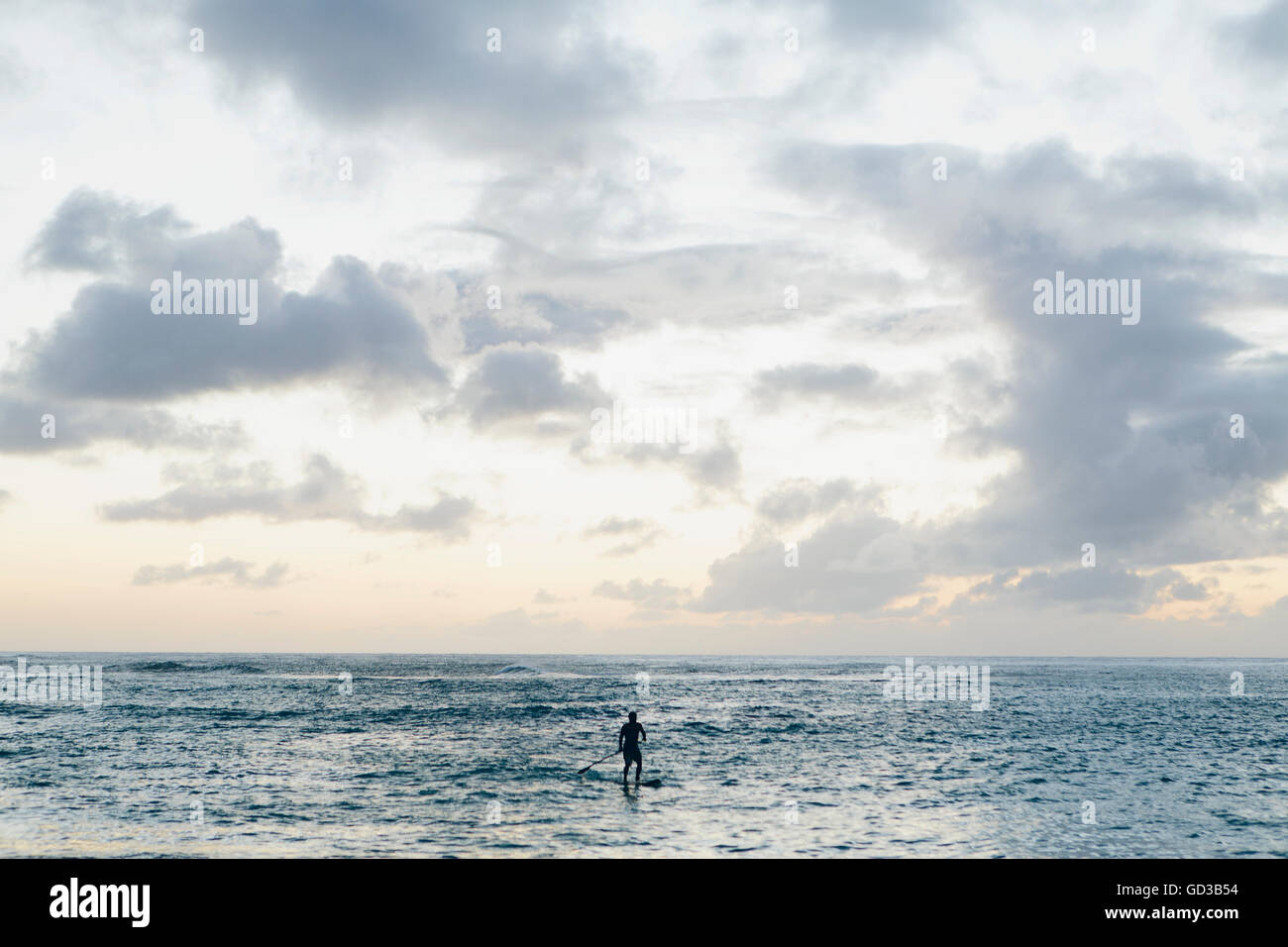 Man stand up paddling in calm waters at dusk Stock Photo