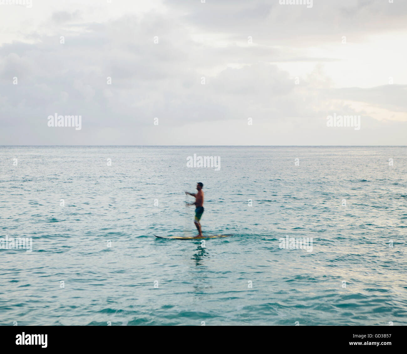 Man stand up paddling in calm waters at dusk Stock Photo