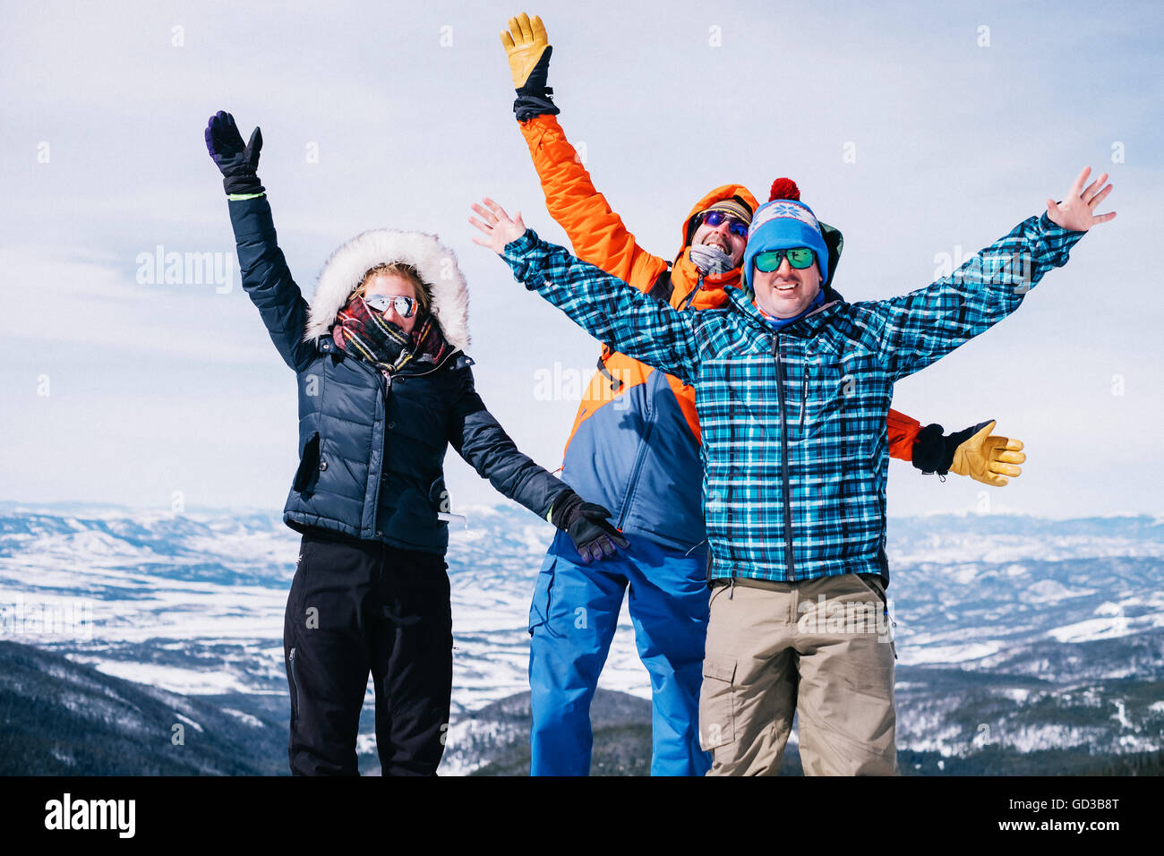 Three people, two men and a young woman standing on top of a mountain with arms outstretched. Stock Photo