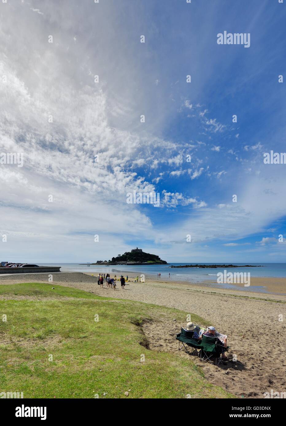 An elderly senior couple sitting on Marazion beach reading newspapers with St Michael's Mount in the background Cornwall England Stock Photo