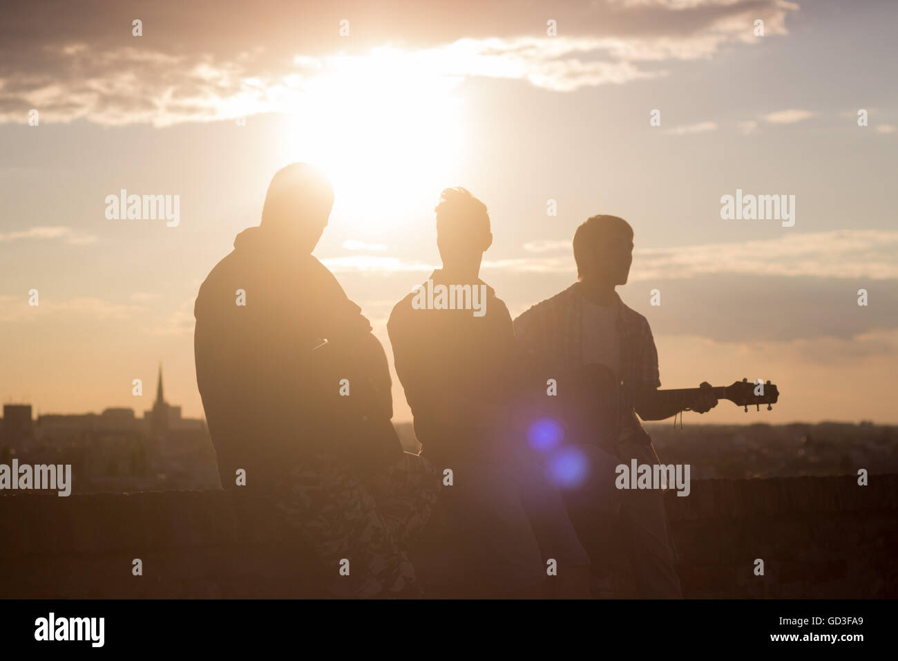 Three men music band backlit guitar. Strong lens flare sunlight sun. Warm colors yellow orange Stock Photo