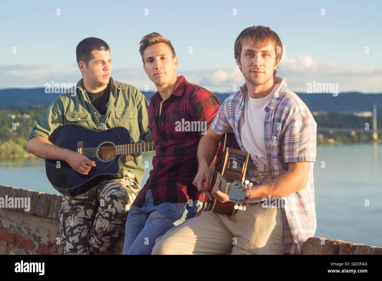 Three men casual music band playing with two guitars and singer, on a sunny day. Stock Photo