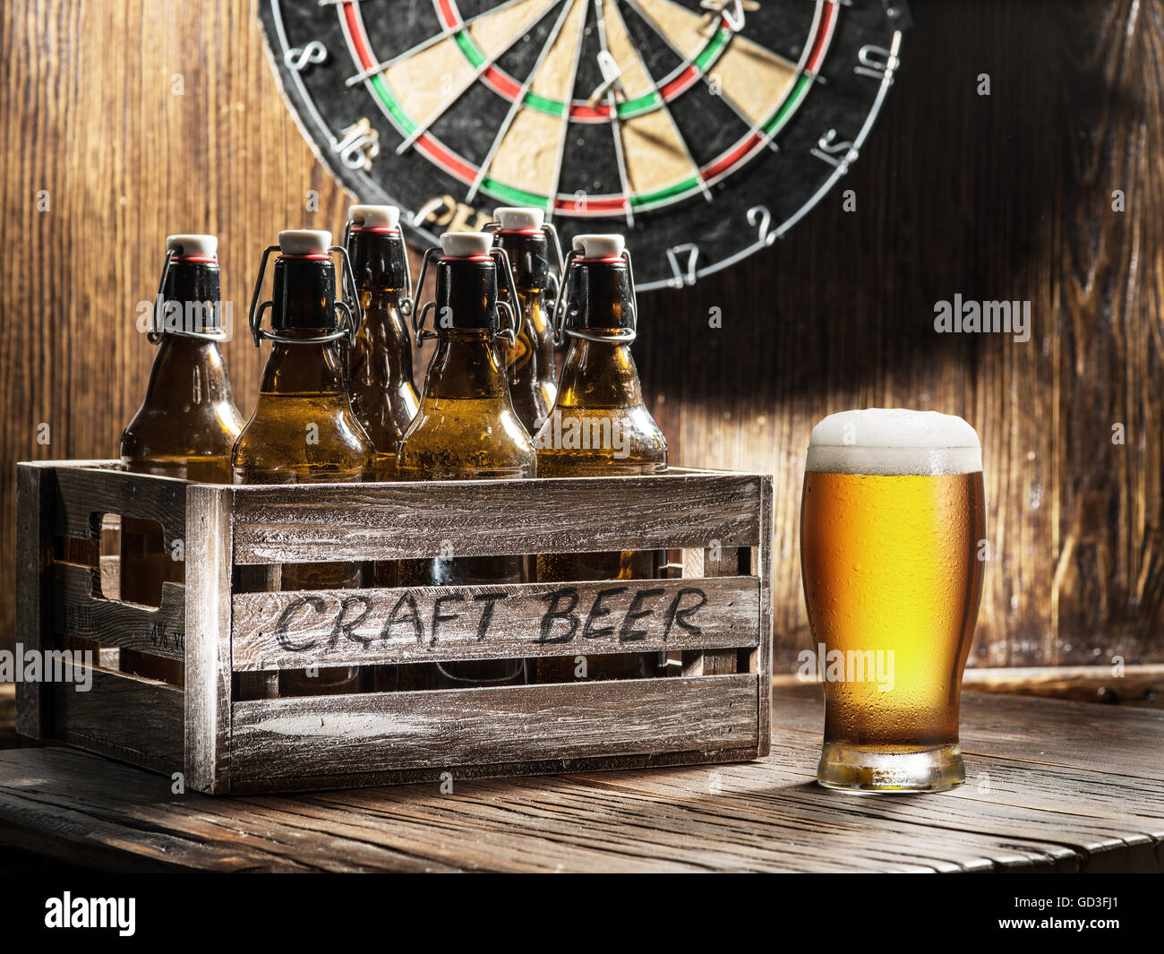 Crafting beer in bottles and glasses. On a wooden wall hangs game of darts. Stock Photo