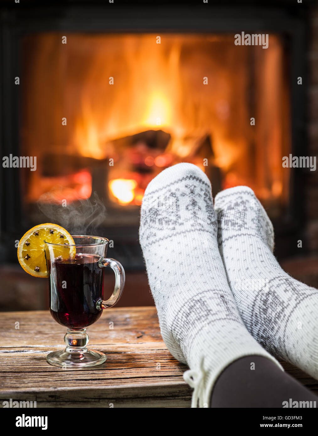 Warming and relaxing near fireplace. Woman feet near the cup of hot wine in front of fire. Stock Photo