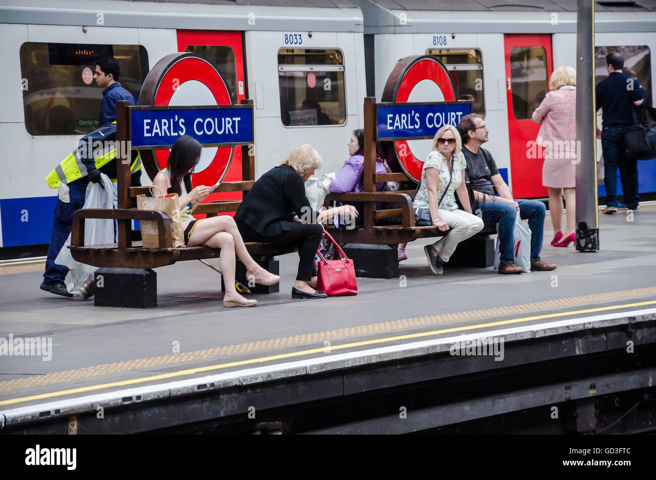Passengers sit on benches at Earl's Court London Underground Station while waiting for their train. Stock Photo