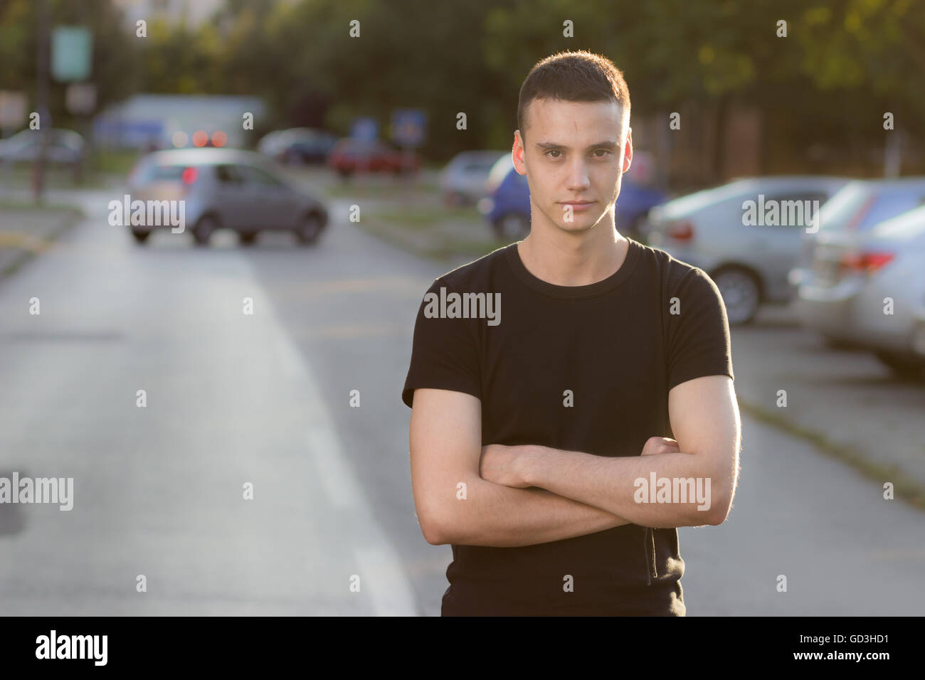 Young man in 20s serious expression, arms crossed. Background out of focus. Stock Photo