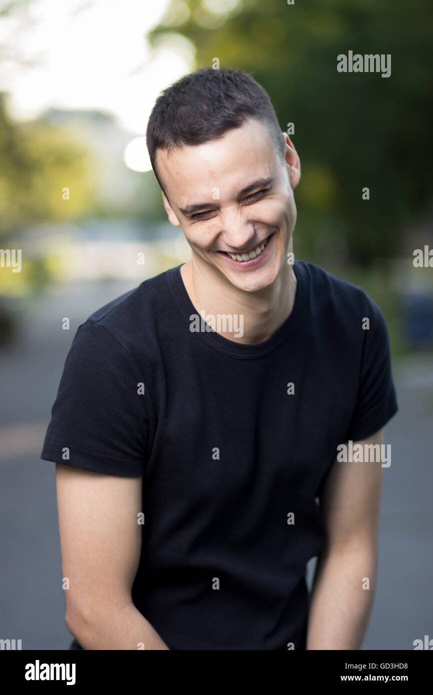 Upper body shot of guy smiling outdoors. Shallow depth of field, background out of focus. Stock Photo