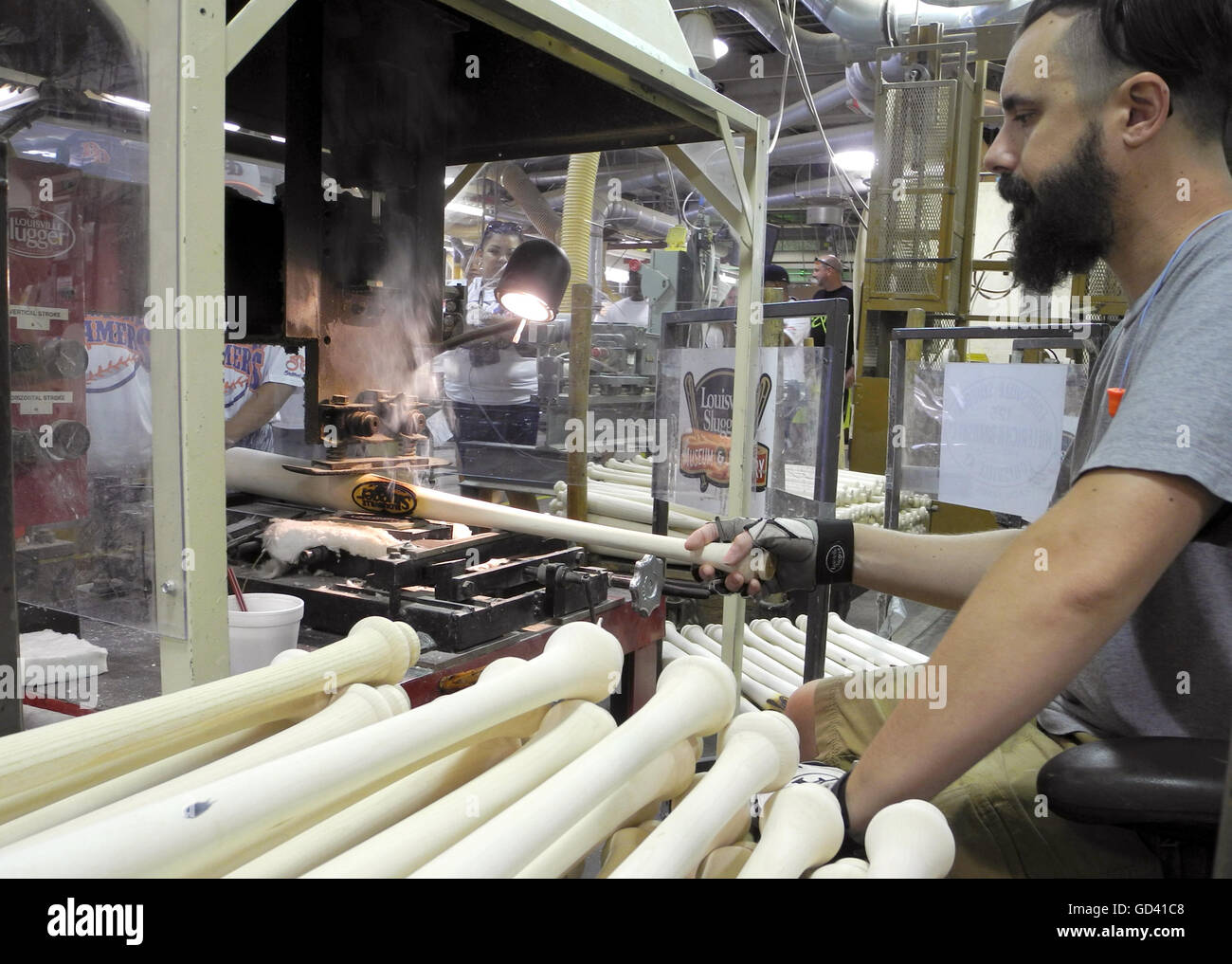 A factory worker burning the Slugger logo into a baseball bat at the