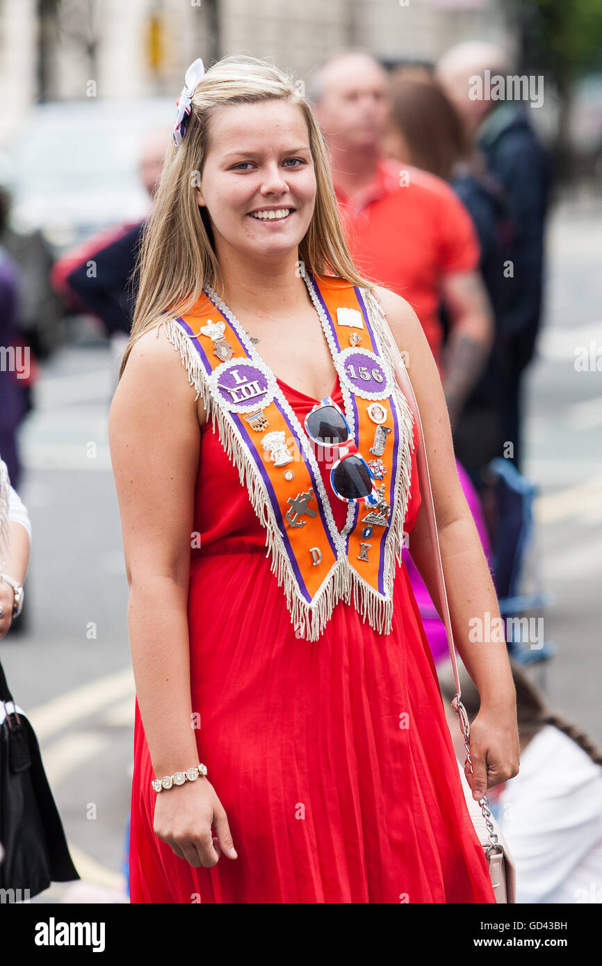 Belfast, UK. 12th July 2016. A Orangewoman wearing a Loyal Orange order Collarette in red dress smiling celebrating the Twelfth. It originated during the late 18th century in Ulster. It celebrates the Glorious Revolution (1688) and victory of Protestant king William of Orange over Catholic king James II at the Battle of the Boyne (1690) Credit:  Bonzo/Alamy Live News Stock Photo